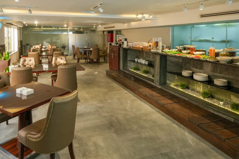 Restaurant dining area with brown leather chairs and a long buffet counter displaying assorted dishes and plates on the right.