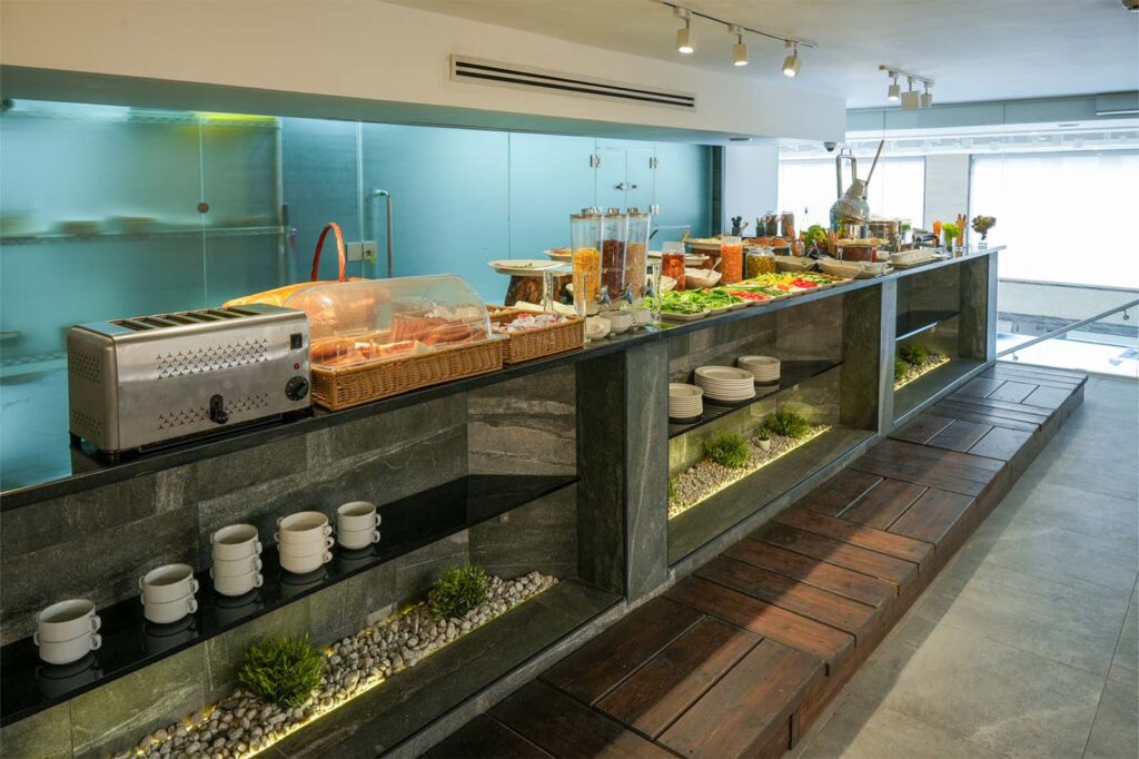 Buffet counter with toaster, wicker bread basket, cereal dispensers, and fresh salad spread in a modern hotel dining area