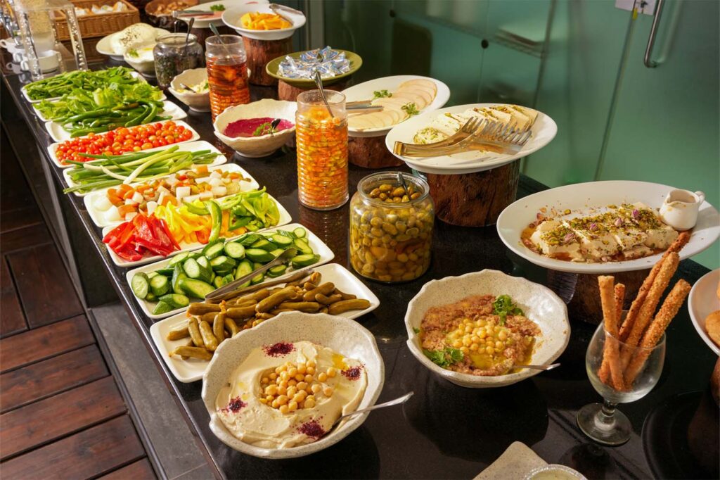 Buffet spread with colorful vegetable platters, dips, olives, and breadsticks lined up on a long counter.