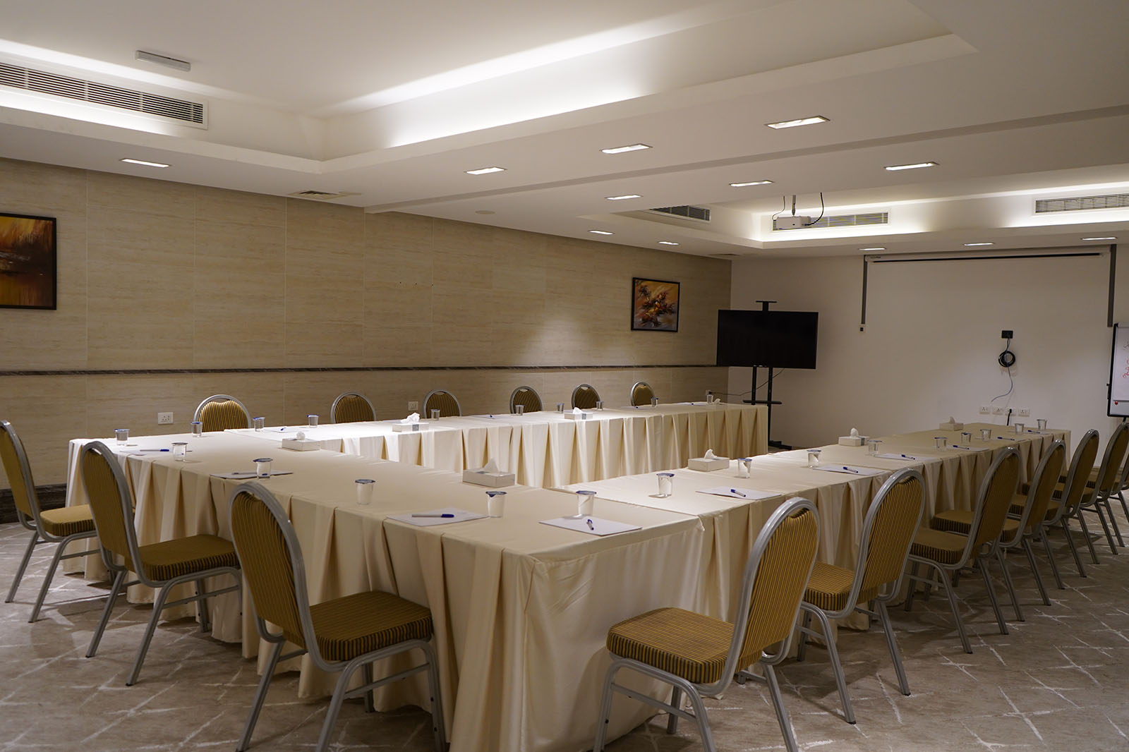 Conference room set up for a meeting with a U-shaped table layout, beige tablecloths, and rows of chairs lined around the room.