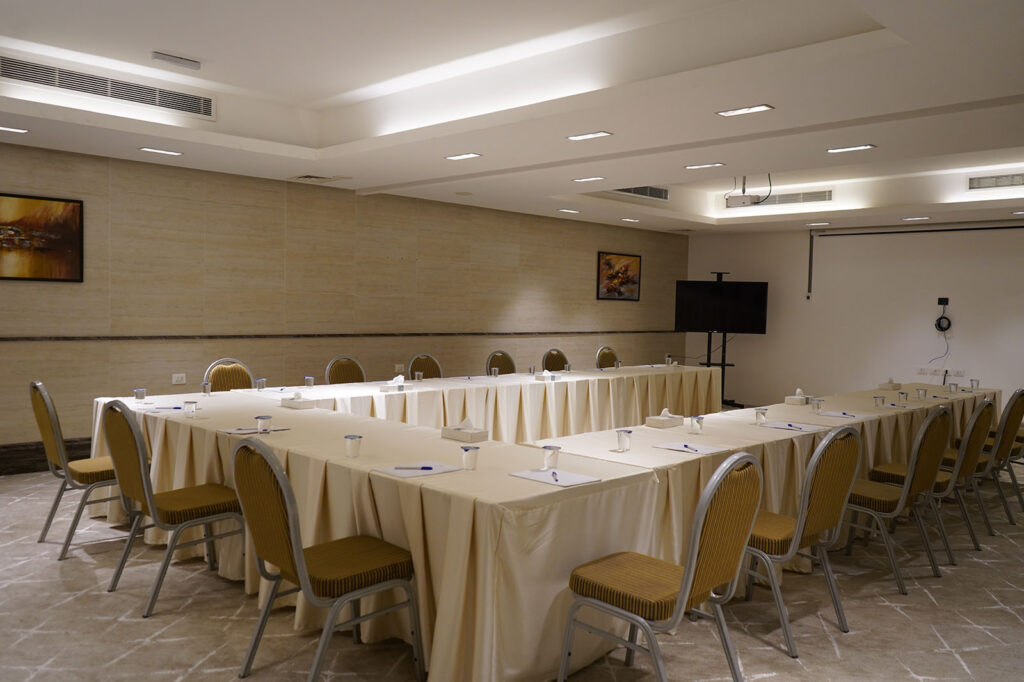 U-shaped conference room setup with beige tablecloths, yellow chairs, notepads and cups on tables, ready for a meeting