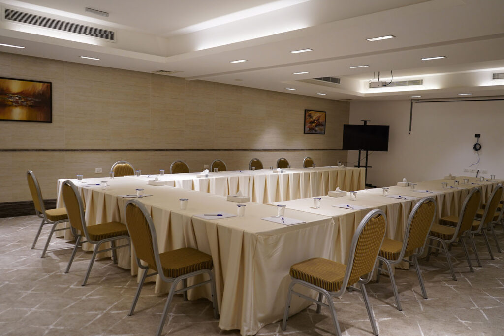 U-shaped conference table setup in a beige-toned room, with chairs, notepads, and cups ready for a meeting.