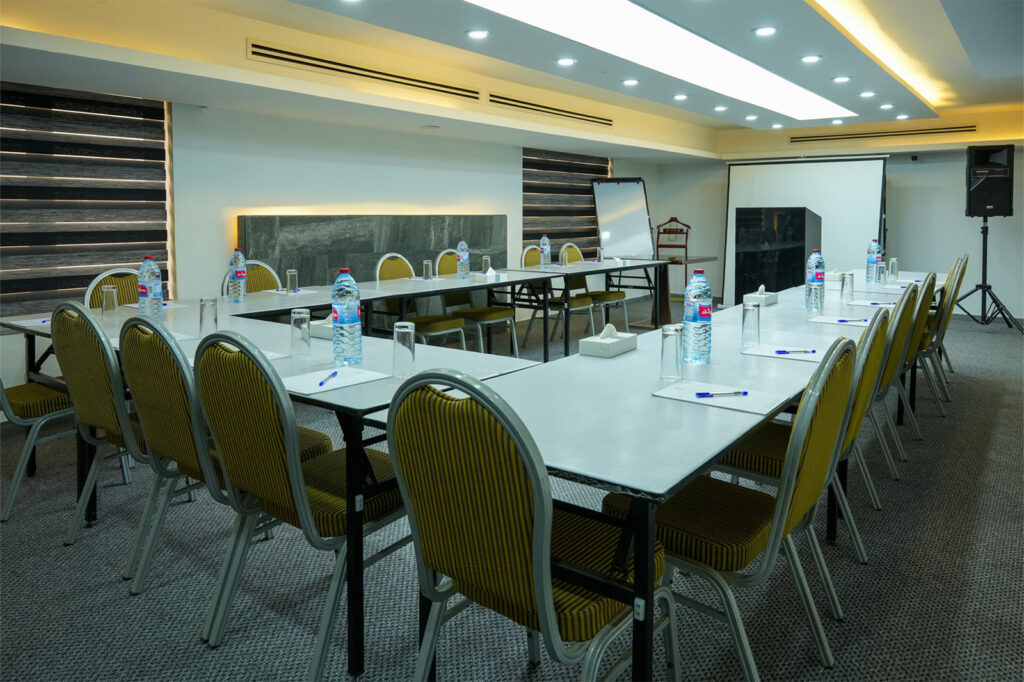 Conference room set up in a U-shaped table arrangement with yellow striped chairs, water bottles, glasses, and pens for a meeting.